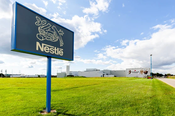 Fachada da fábrica da Nestlé com placa da empresa em destaque sob céu azul.